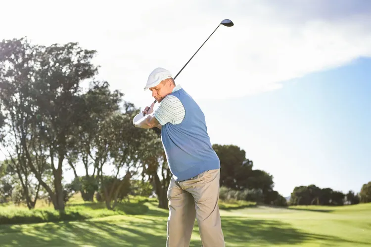 Man in golf attire tees off on the sunny Schloss Karnitz golf course while on vacation at the Grand Hotel Binz.
