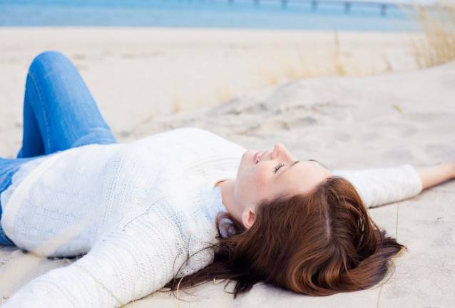 A woman lies on the beach in Binz with her arms outstretched, enjoying the Baltic Sea breeze.