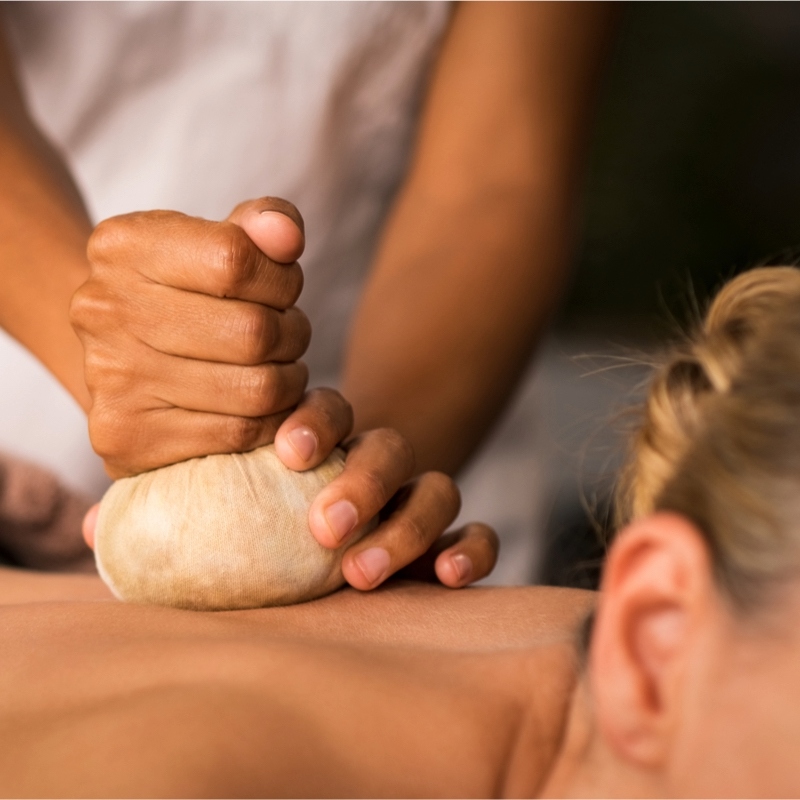 Nahaufnahme einer Frau bei einer wohltuenden ayurvedischen Kräuterstempelmassage auf dem Rücken.