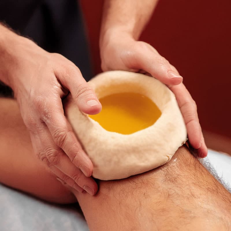 Ayurveda-Teigring an einem Knie, gefüllt mit beruhigendem Kräuteröl.