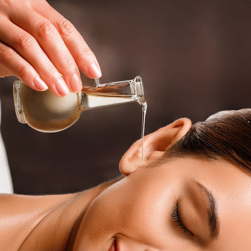 Kräuteröl fließt in das Ohr eines zufrieden lächelnden Spa-Gastes.