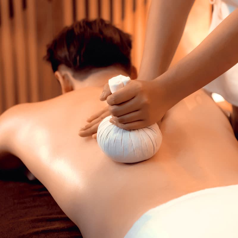 Anwendung einer lösenden Kräuterstempelmassage am Rücken eines Mannes.
