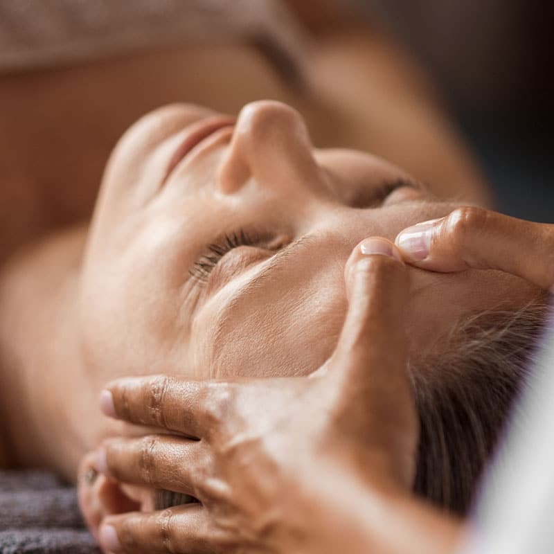 Gezielte, wohltuende Massagegriffe am Kopf eines entspannten Gastes.