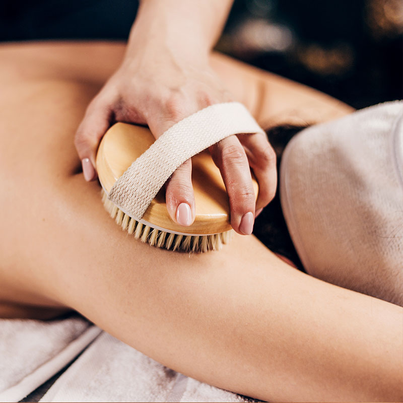 Dry brushing full body massage with copper bristles on a customer's arm to stimulate blood circulation.