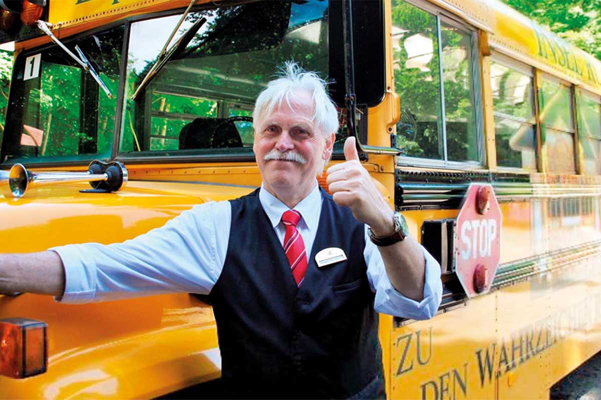Ein freundlicher Fahrer vor einem nostalgischen Schulbus vorm Grand Hotel Binz, bereit zur Abfahrt zum Kap Arkona.