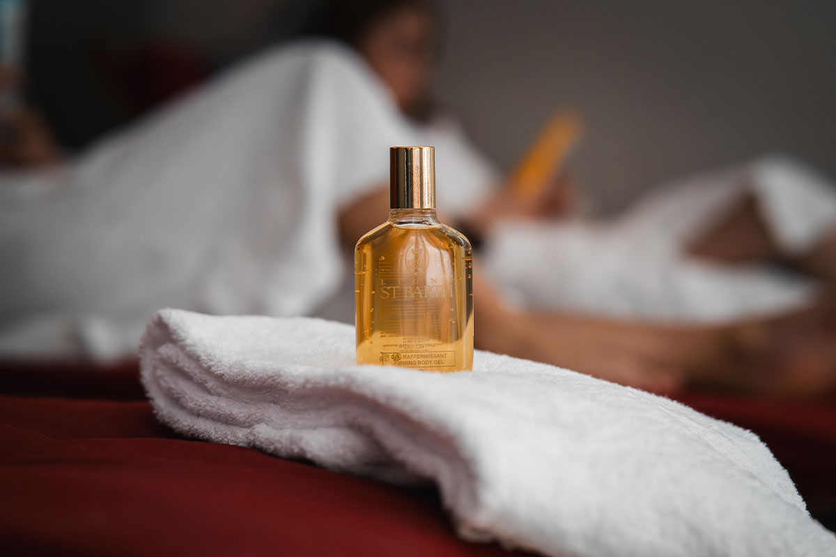 Goldenes Fläschchen von Ligne St. Barth auf weißem Handtuch, im Hintergrund Spa-Gäste