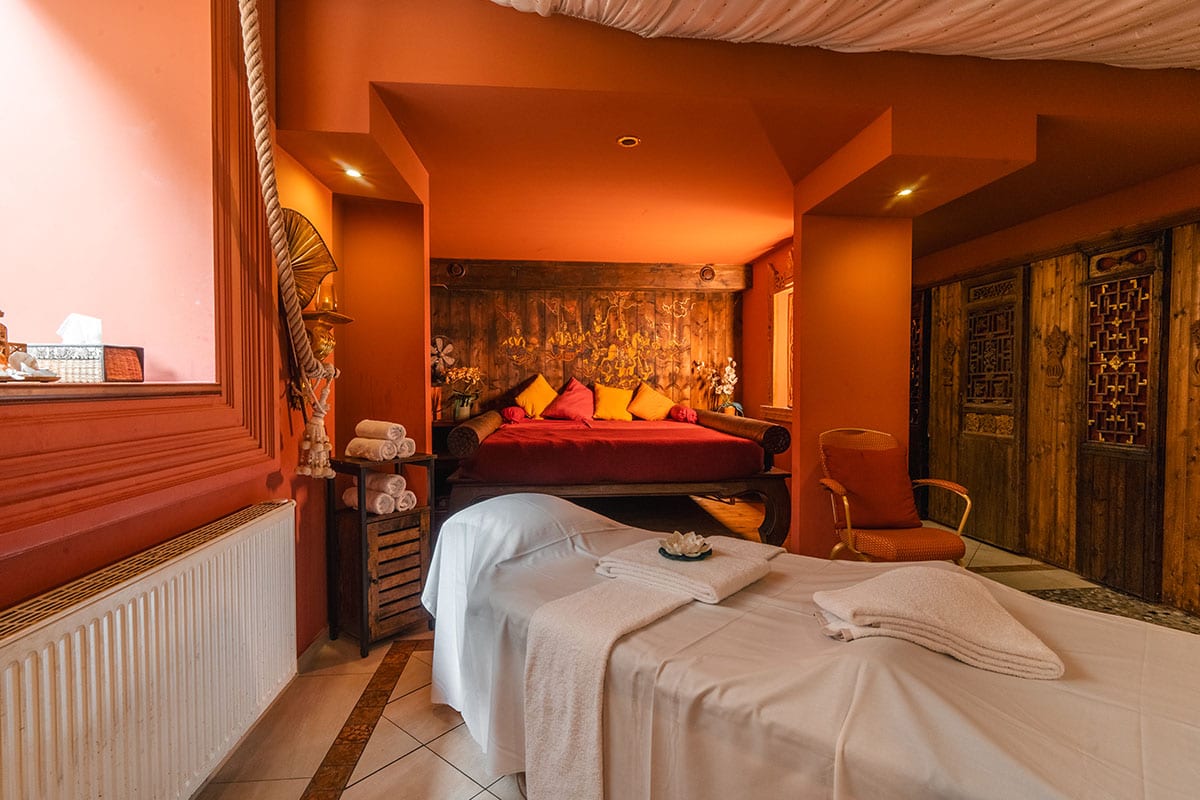 Weiß bezogene Behandlungsliege im Spa mit rotem Tagesbett und asiatischer Dekoration